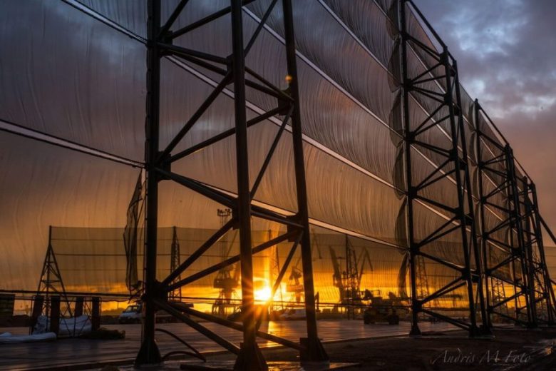 A large industrial structure with translucent panels stands against a vibrant sunset