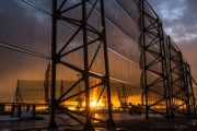 A large industrial structure with translucent panels stands against a vibrant sunset