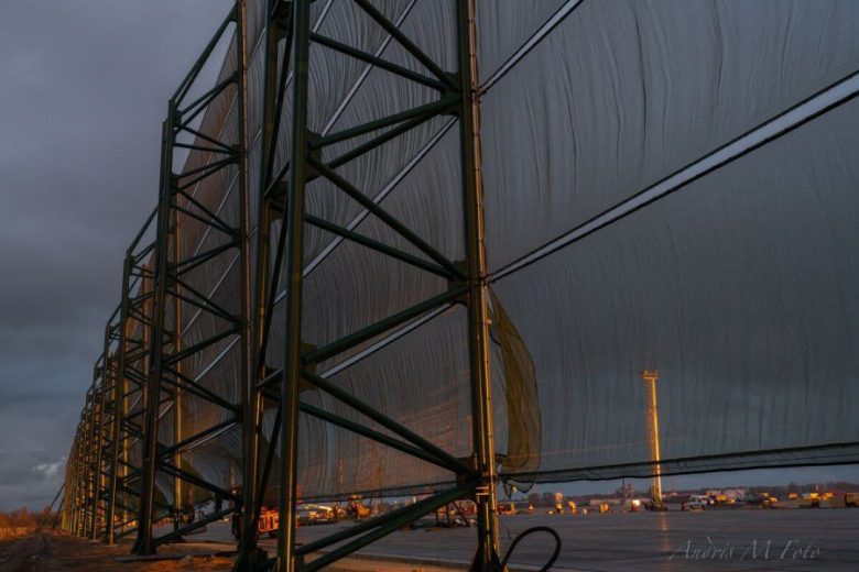 A large industrial wind fence structure stands against a dark, cloudy sky