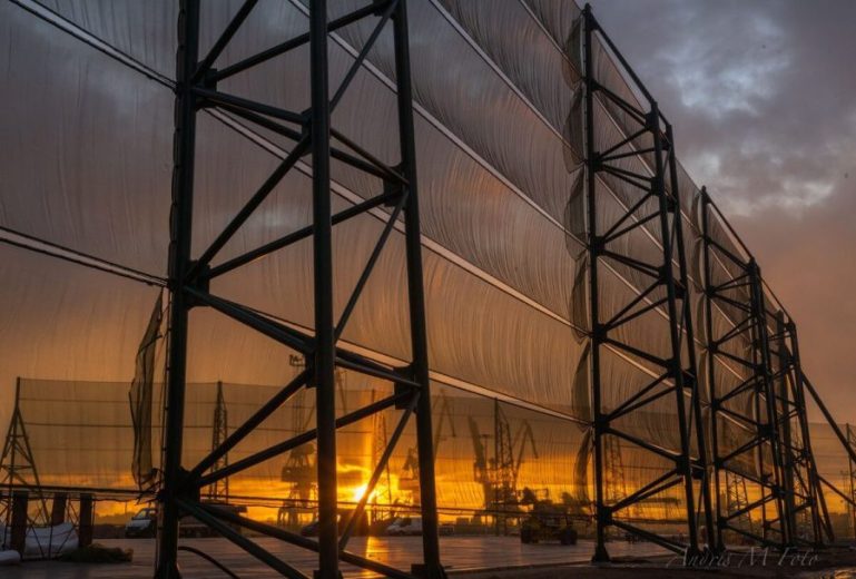 A large industrial wind fence with a sunset visible through the mesh panels