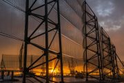 A large industrial wind fence with a sunset visible through the mesh panels