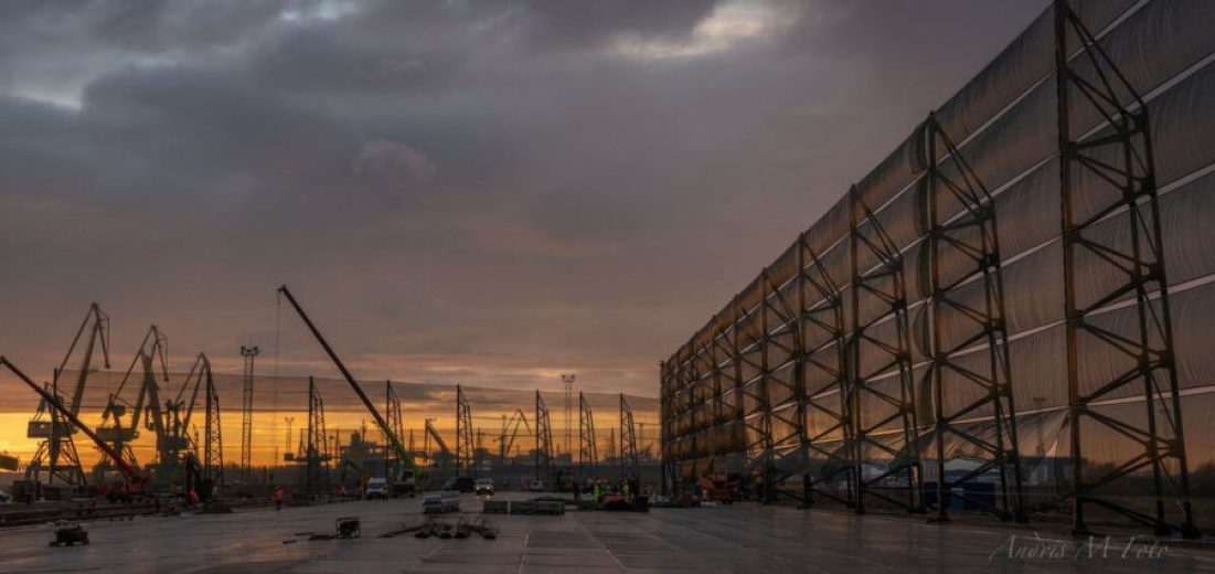 A large industrial site with cranes and a long wind fence at sunset