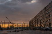 A large industrial site with cranes and a long wind fence at sunset