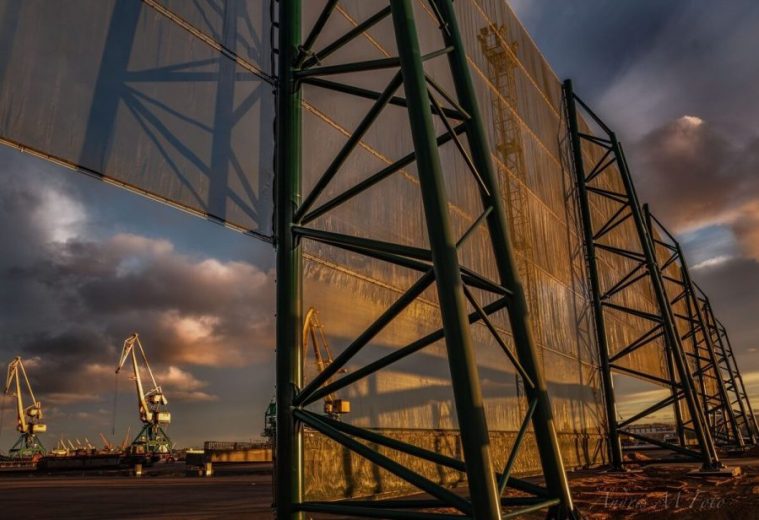 Large industrial wind fence structure with cranes in the background at sunset
