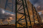 Large industrial wind fence structure with cranes in the background at sunset