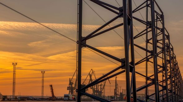 A steel structure stands tall against a vibrant sunset sky at an industrial site