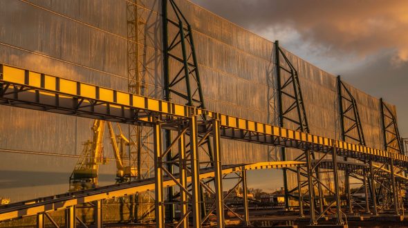 A large industrial structure with metal framework and translucent panels, reflecting a sunset