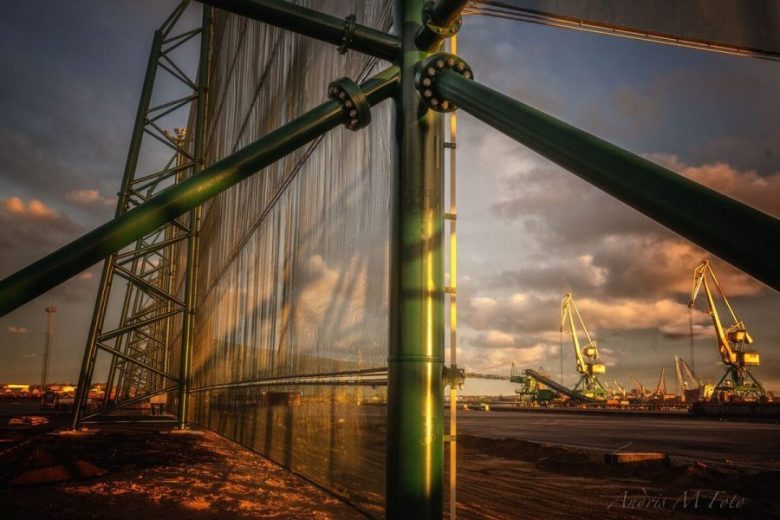 A large industrial wind fence with cranes in the background at sunset