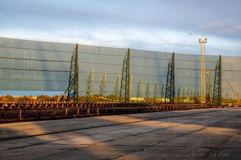 A long industrial wind fence stretches across a paved area with metal supports