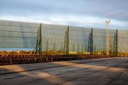 A long industrial wind fence stretches across a paved area with metal supports