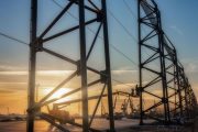 A large metal structure with workers on a lift against a sunset backdrop