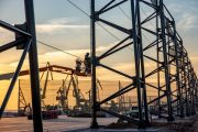 A worker in a lift basket installs a metal framework against a sunset backdrop