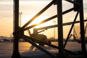A construction vehicle silhouetted against a sunset, framed by metal beams