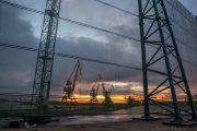 Cranes silhouetted against a sunset, viewed through a metal framework and netting