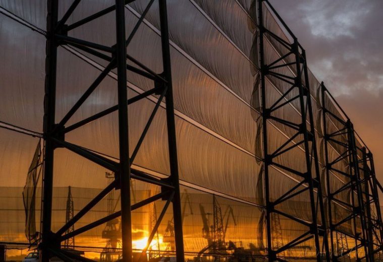 A large industrial fence structure with translucent panels against a sunset sky