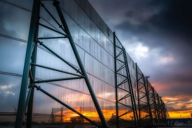 A large industrial wind fence stands against a dramatic sunset sky