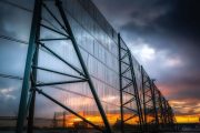 A large industrial wind fence stands against a dramatic sunset sky