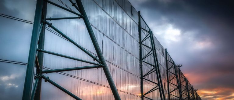 A large industrial fence structure stands against a dramatic sunset sky