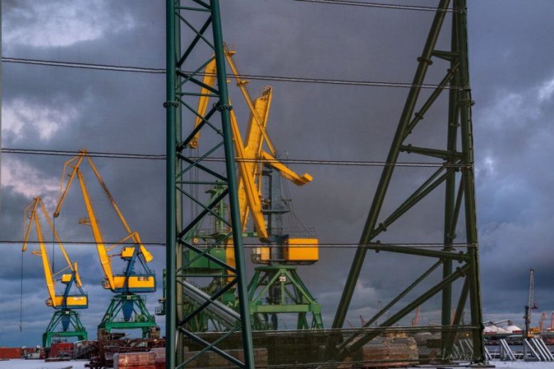 Yellow and green cranes stand behind a green metal fence under a cloudy sky