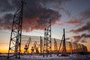 Industrial wind fences stand against a dramatic sunset with silhouetted cranes in the background