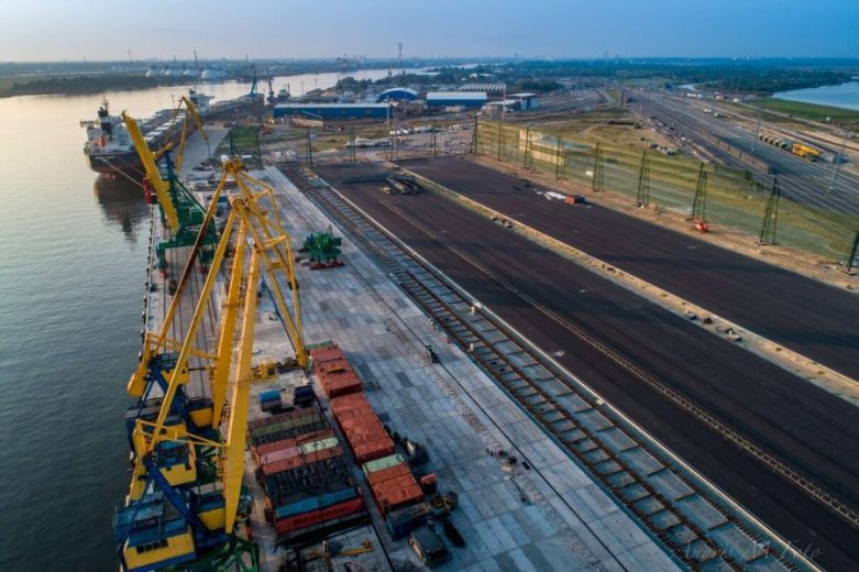 Aerial view of a port with cranes, shipping containers, and adjacent railway tracks