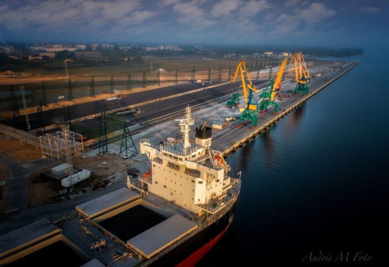 Aerial view of a cargo ship docked at an industrial port with cranes and infrastructure