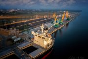 Aerial view of a cargo ship docked at an industrial port with cranes and infrastructure