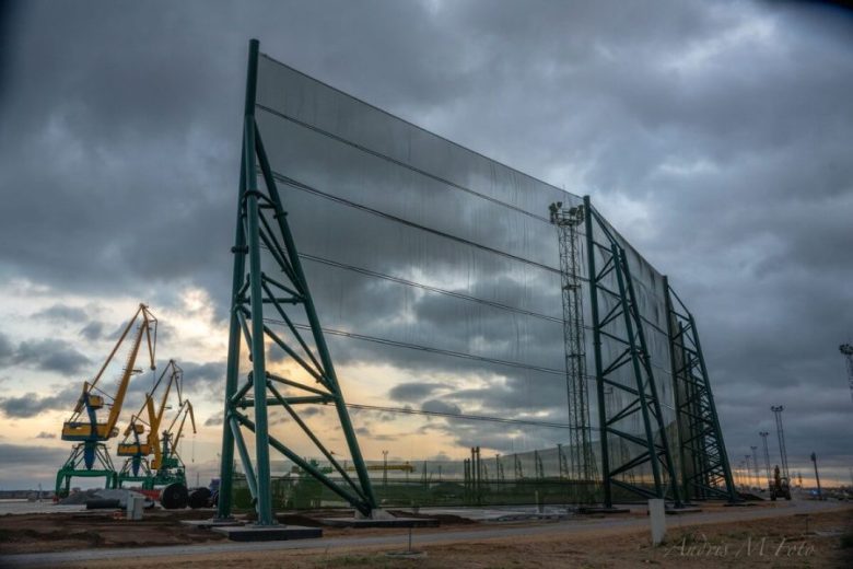 Large industrial wind fence with cranes in the background under a cloudy sky
