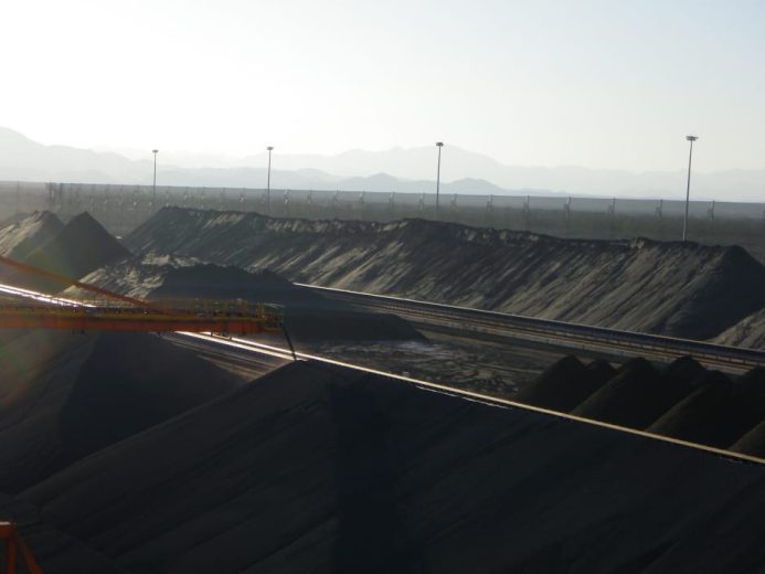 Large piles of dark material with a crane and mountains in the background
