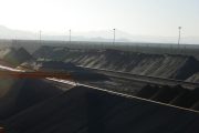 Large piles of dark material with a crane and mountains in the background