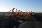 Large industrial machinery operates among massive piles of dark material under a clear sky