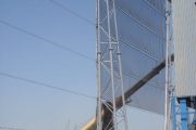 A tall industrial wind fence with workers and machinery at the base under a clear sky