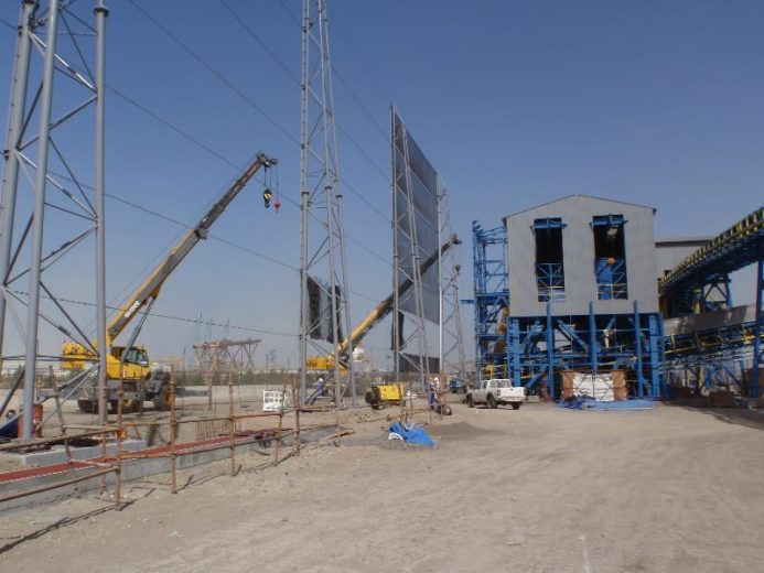 Construction site with cranes, scaffolding, and a large industrial building under a clear sky