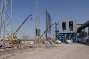 Construction site with cranes, scaffolding, and a large industrial building under a clear sky