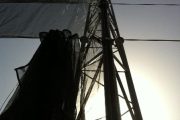 A tall metal structure with netting against a bright sky, likely a windbreak or canopy