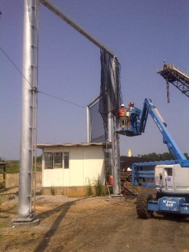 Construction workers install a large metal windbreak fence with a crane and lift